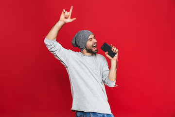 Canvas Print - Image of optimistic man 30s singing while listening to music with earphones and mobile phone, isolated over red background