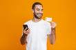 © Drobot Dean - Photo of joyful man 30s in casual wear holding smartphone and credit card, isolated over yellow background