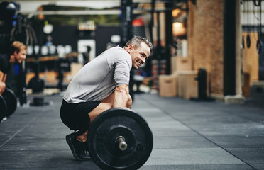 Wall Mural - Smiling man preparing to lift weights at the gym