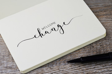 welcome change hand lettering in notebook with pen on wooden background