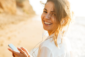 Sticker - Beautiful young woman walking outdoors at the beach using mobile phone.