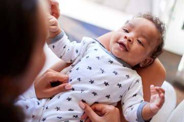 happy three month old baby boy lying on his back on his motherâ€™s knee looking up at her, over shou