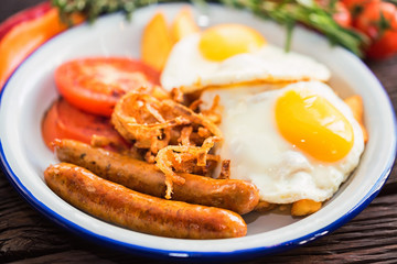 Typial breakfast with eggs, tomato, onion rings and sausage on plate