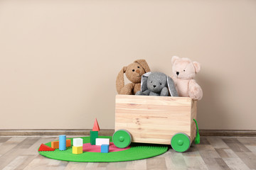 Wall Mural - Wooden cart with stuffed toys and constructor on floor against light wall. Space for text