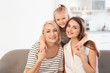 © New Africa - Portrait of young woman, her mature mother and daughter on sofa in living room