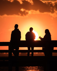 Wall Mural - Silhouette of young adults on a fishing pier watching the sunset. Hanging out with friends, enjoying nature. Long Island New York.  