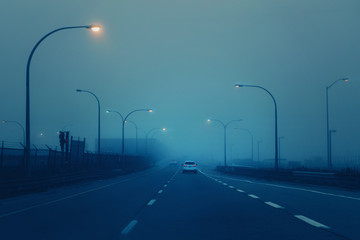 Highway in mystic fog mist smog. Cars on freeway road at evening in american city country. Poor visibility in bad weather conditions. Toned with retro film hipster filters. Dangerous suspense