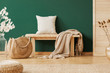 © Photographee.eu - Wooden bench with beige carpet and pillow next to straw handbag, copy space on the empty green wall