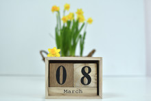 8 March Composition On White Background. March 8 Text On Wooden Block Calendar And One Flower Of Yellow Narcissus .basket Of Daffodils In The Background