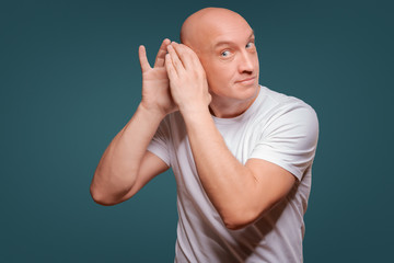 Wall Mural - a man on a blue background in holding his hands near his ear, eavesdropping