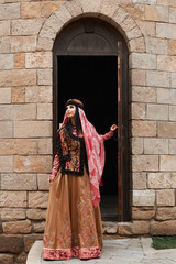 Beautiful girl in traditional dress comes out of the door of a brick house