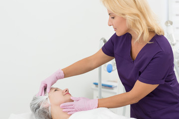 Wall Mural - View from side of qualified beautician in process of examining skin of patient lying on couch. Female doctor in uniform and gloves in process doing hardware procedure. Concept of skin care and beauty.