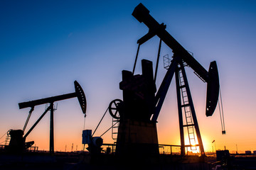 Oil pumps are running in the sunset at the oil field. The outline of the pumping unit.