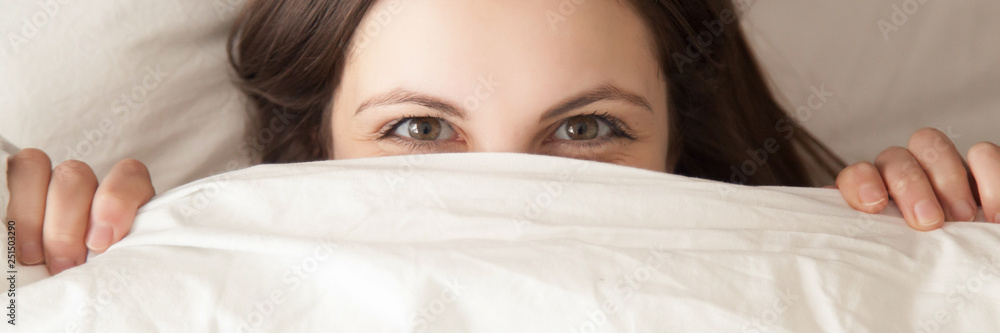 Horizontal image woman hiding under white blanket lying on pillow - obrazy, fototapety, plakaty 