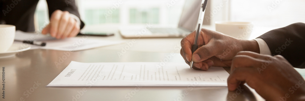 Horizontal closeup image black businessman sitting at desk signing contract - obrazy, fototapety, plakaty 