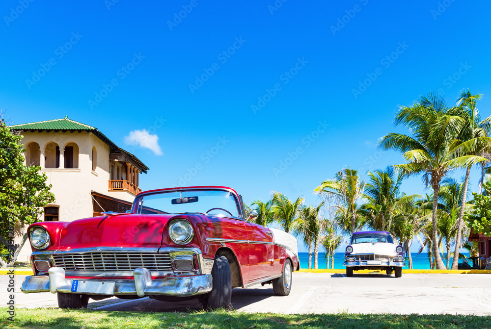 Roter amerikanischer Cabriolet  Oldtimer und ein blau weisser Oldtimer parken am Strand von Varadero in Cuba - Serie Kuba Reportage - obrazy, fototapety, plakaty 