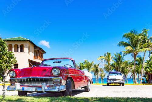  Fototapeta Kuba   klasyczny-czerwony-amerykanski-kabriolet-oraz-niebiesko-bialy-klasyczny-samochod-zaparkowany-na-plazy-przy-ul