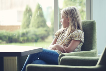 Bored child girl looks out the window on a rainy summer day