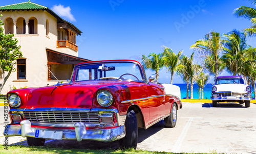  Fototapeta Kuba   klasyczny-czerwony-amerykanski-kabriolet-oraz-niebiesko-bialy-klasyczny-samochod-zaparkowany-na-plazy-przy-ul