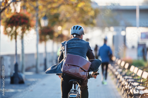 Cuadros en Lienzo A rear view of businessman commuter with electric bicycle traveling to work in city