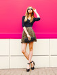 © rohappy - Fashionable young blonde woman in leopard skirt, sunglasses with handbag clutch posing on city street over colorful pink wall background