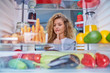 Woman standing in front of fridge full of groceries and taking juice. Picture taken from inside of fridge.