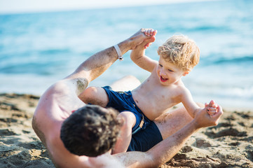 A father with a toddler son playing on sand beach on summer holiday.