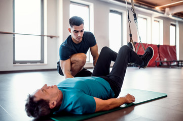 Sticker - A senior man in gym and a personal trainer doing exercise with TRX.
