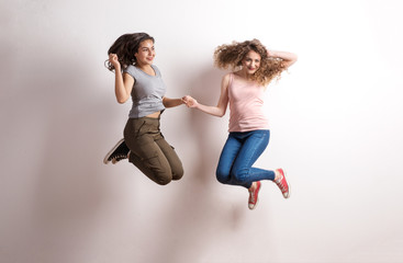 Wall Mural - Two young beautiful women in studio, jumping.