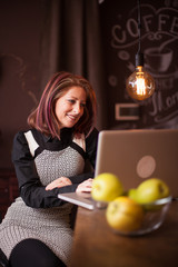 Wall Mural - Businesswoman smiling while looking at her laptop in a vintage coffee shop