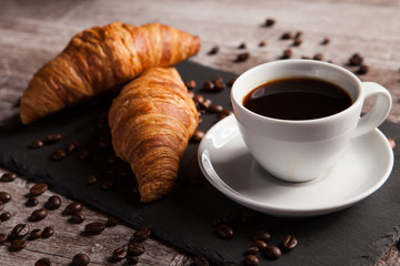 Two fresh croissants and cup of coffee on dark stone table