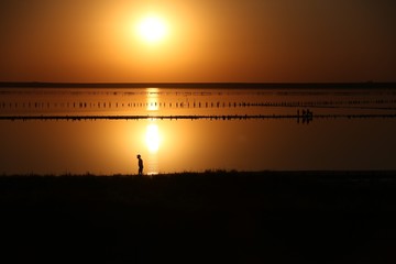 On a salt lake in the setting sun, family, father with a hat, mother and small child on the horizon with a silhouette walk along the shore