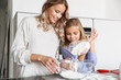 © Drobot Dean - Woman with her little sister indoors at home kitchen cooking with flour.