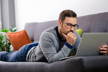 Wall Mural - Handsome young man studying something on his laptop while lying