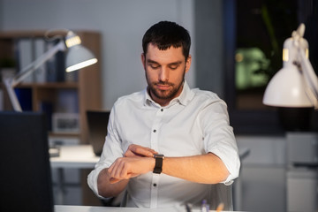 Wall Mural - business, technology and time management concept - happy smiling businessman with smart watch at nig