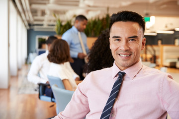 Portrait Of Businessman In Modern Office With Colleagues Meeting Around Table In Background