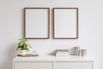 Poster - Minimalistic home decor of interior with two brown wooden mock up photo frames on the white shelf with books, beautiful plant in stylish pot and home accessories. White wall. 