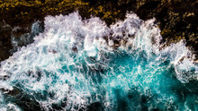 Aerial View To Ocean Waves. Blue Water Background - Top Vertical View Of Coastline And Big Power Waves On The Rocks - Splash And Dangerous Concept For Nature Outdoor Beauty