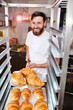 © Evgeniy Kalinovskiy - A young handsome male baker holds a tray with French croissants in front of a bakery and smiles.