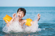 © marina_larina - Happy smiling boy bathes in the sea near the shore with splashes of water. Wet hair. Orange inflatable swim sleeves. A child at the sea, rest in the summer, swimming in the sea. Summer school holidays