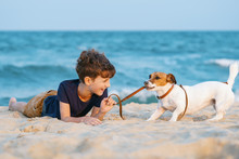 Happy Boy Hugging His Dog Breed Jack Russell Terrier At The Seashore Against A Blue Sky Close Up At Sunset. Best Friends Rest And Have Fun On Vacation, Play In The Sand Against The Sea Summer