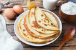 Thin pancakes on a plate. Wooden background. Ingredients to cooking eggs, milk, flour.