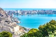 The view from the fort of Alicante, Spain, showing the city below, with the blue water of the Mediterranean in the bay below and on the far-side of the city.