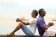 © Erickson Stock - Happy mature couple sitting back to back by the beach.