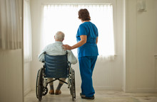 Female Nurse Comforting A Senior Man Sitting In A Wheelchair.
