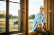 © Erickson Stock - Expectant mother sitting in the window frame of a home under construction.