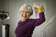 © Erickson Stock - Smiling senior woman flexing her muscles while standing on scales.