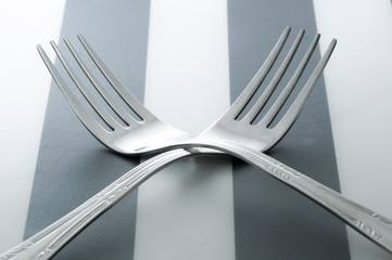 Two forks cross on striped background. 2 forks laying next to each other.