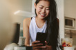 © Jacob Lund - Smiling female with smartphone in kitchen in morning