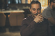 © Nestor - Businessman wearing in dark shirt sitting in bar and tasting elite alcohol. Confident man smiling and looking away. Client of bar holding glass with strong drink
